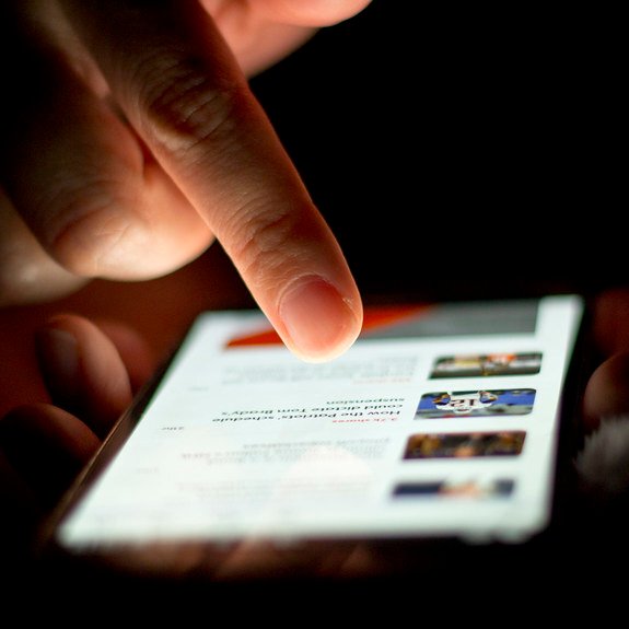 En pekefinger beveger seg over en synlig liste med nyhetsartikler på en smarttelefonskjerm.